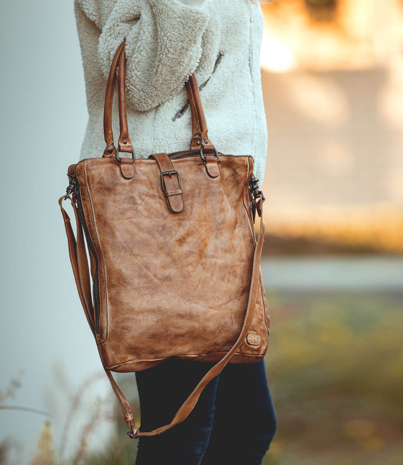 A woman holding a Bed Stu Mildred brown leather tote bag.