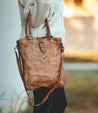 A woman holding a Bed Stu Mildred brown leather tote bag.