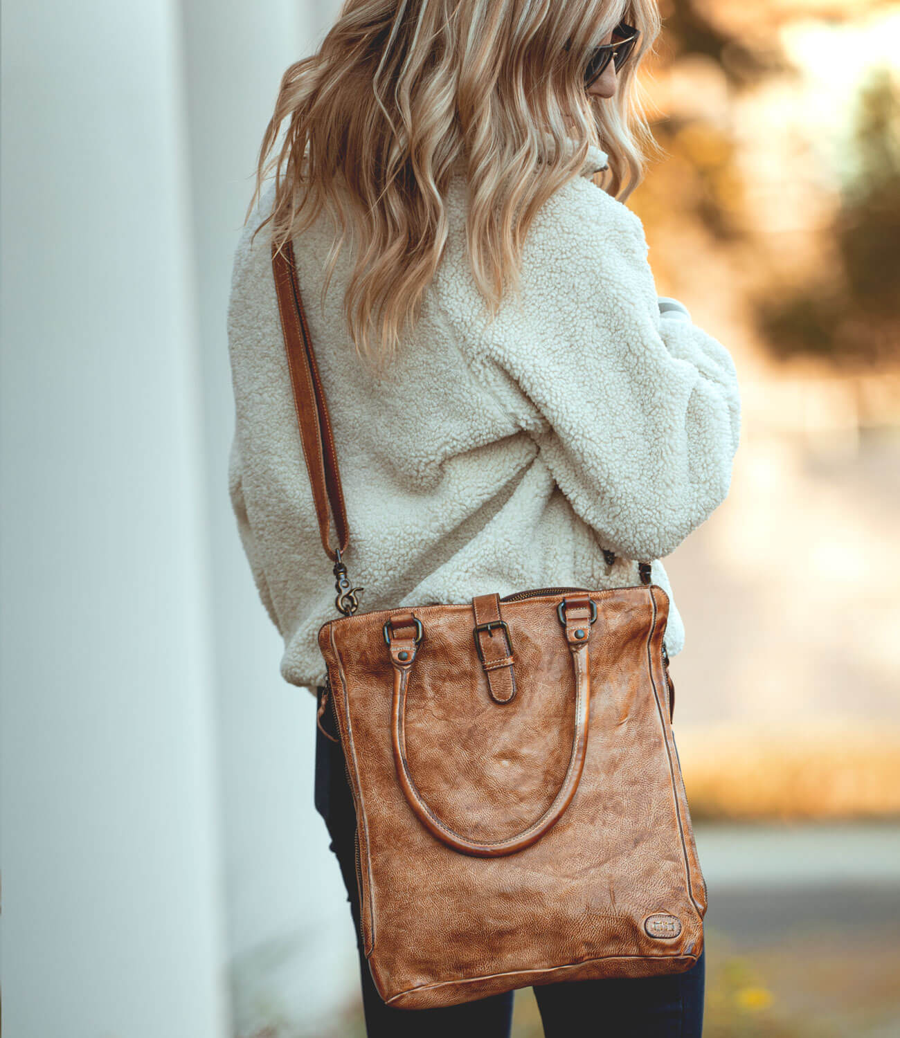 A woman wearing jeans and a sweater holding a Mildred tote bag by Bed Stu.