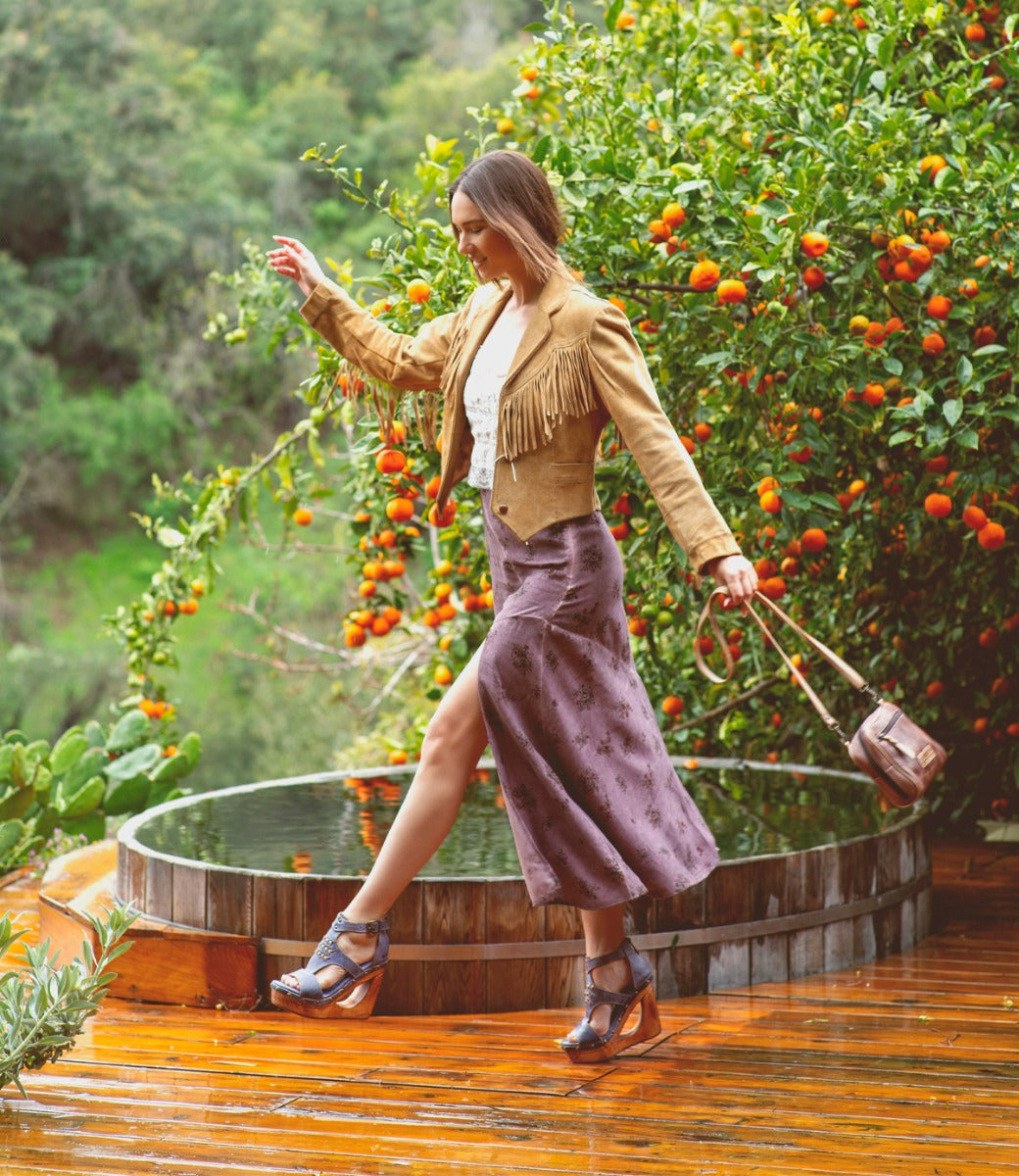 A woman walking on a Millennial deck with an orange tree in the background. Brand name: Bed Stu.