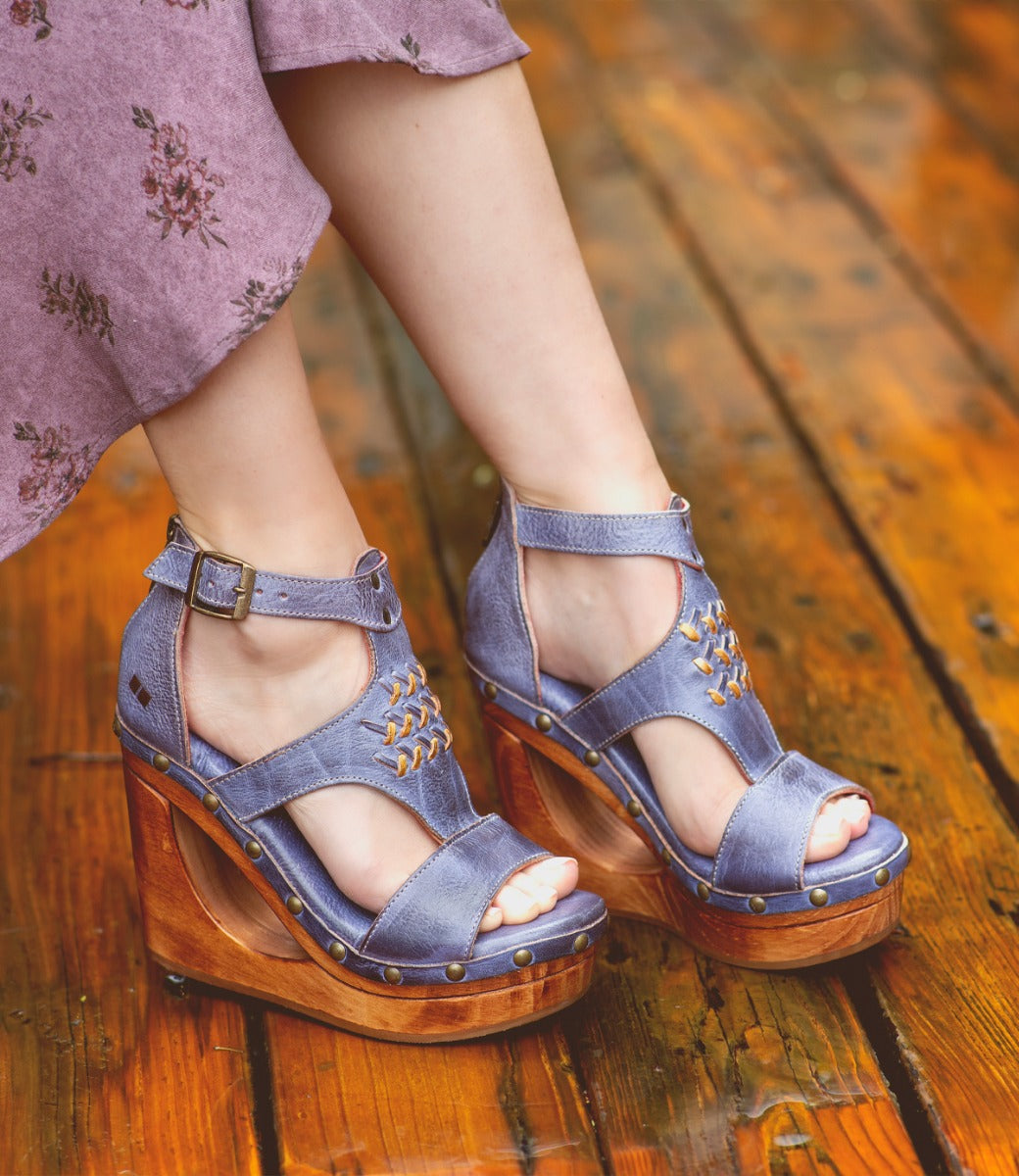 A woman is standing on a wooden deck wearing a pair of Bed Stu Millennial wedges.