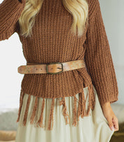 A person wearing the Bed Stu Mohawk brown textured sweater with a fringe hem, paired with a women's distressed light brown leather belt and a cream skirt.
