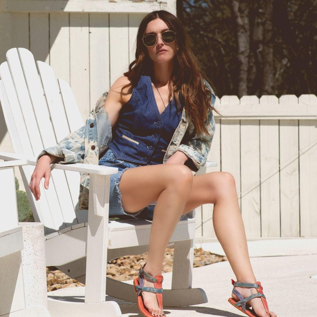 A woman sitting on a white chair wearing Moon sunglasses and a Bed Stu denim jacket.