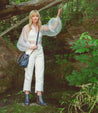 A woman standing in the woods wearing white pants and a pair of Bed Stu Nandi boots.