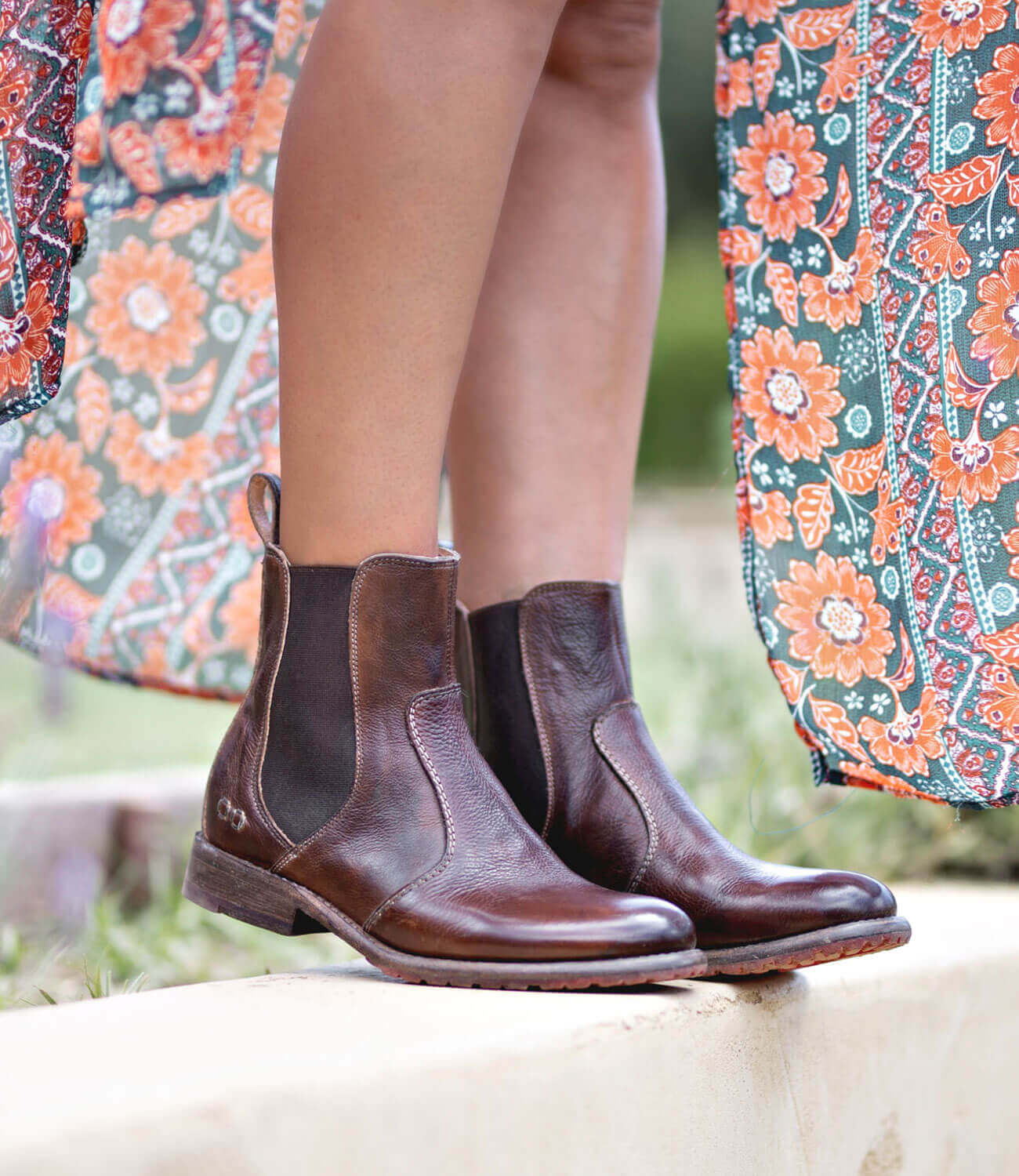 A woman wearing a floral dress and teak Bed Stu Nandi chelsea boots.