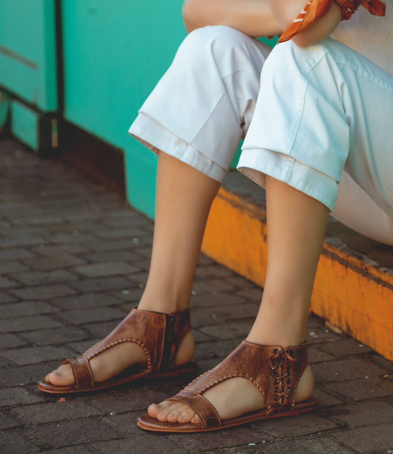 A woman is sitting on a bench wearing Bed Stu sandals.
