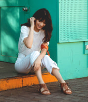 A woman is sitting on a sidewalk talking on her Bed Stu Nina cell phone.