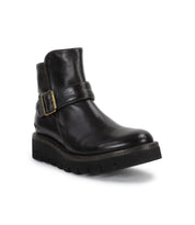 The Bed Stu Nudge II is a black leather ankle boot with an adjustable strap, decorative side buckle, low heel, and thick textured sole, shown on a white background.