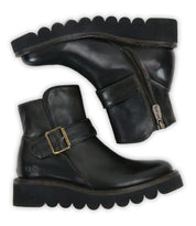Bed Stu’s Nudge II black ankle boots feature leather finishes, side zippers, an adjustable strap, and thick scalloped rubber soles, displayed side by side.