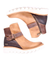 A pair of Bed Stu Nudge II two-tone brown ankle boots with white soles, featuring a side zip and an adjustable strap on each boot. The boots are positioned side by side, facing opposite directions.