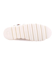 View of the sole of the Nudge II by Bed Stu, a white shoe featuring a ridged, segmented pattern. The design includes textured lines on each segment, offering great grip and visual appeal. This versatile ankle boot boasts an adjustable strap and side zip for added convenience and style.