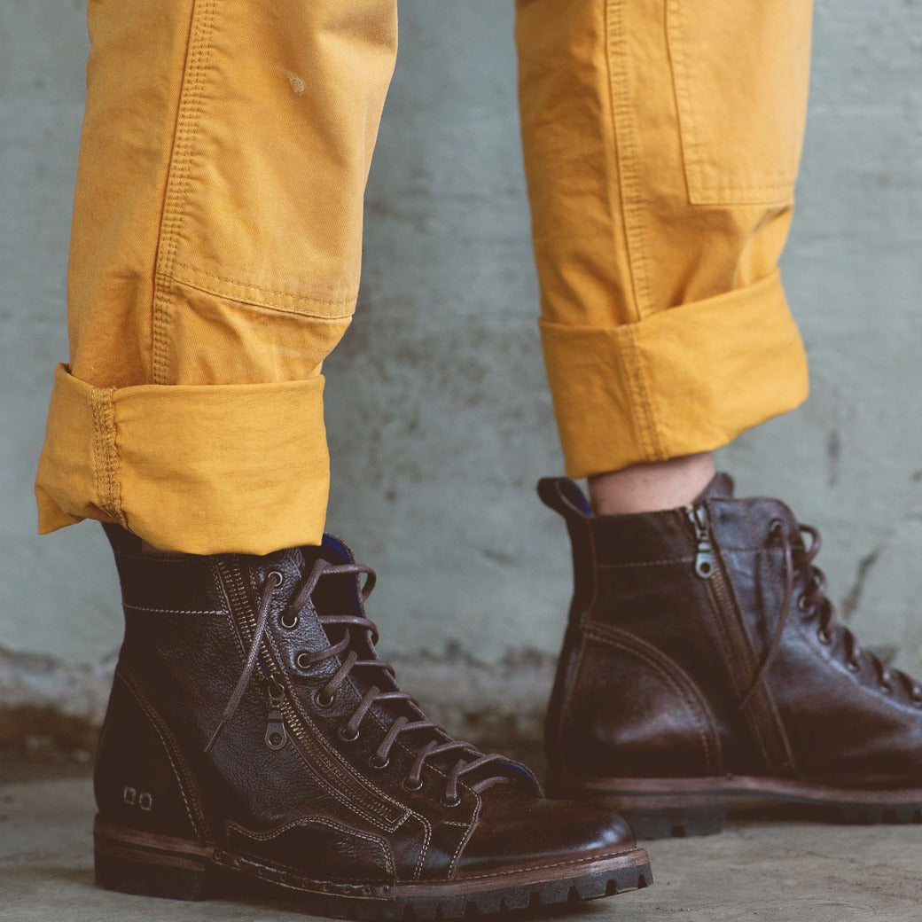 A person wearing a pair of Old Bowen Trek boots by Bed Stu and yellow pants.