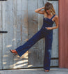 A woman in a Bed Stu denim jumpsuit leaning against a wooden door.