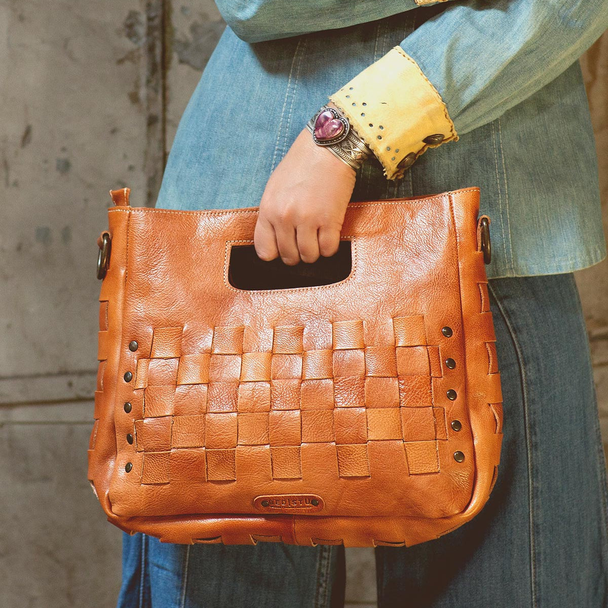 A woman is holding an adjustable handwoven Orchid handbag by Bed Stu.