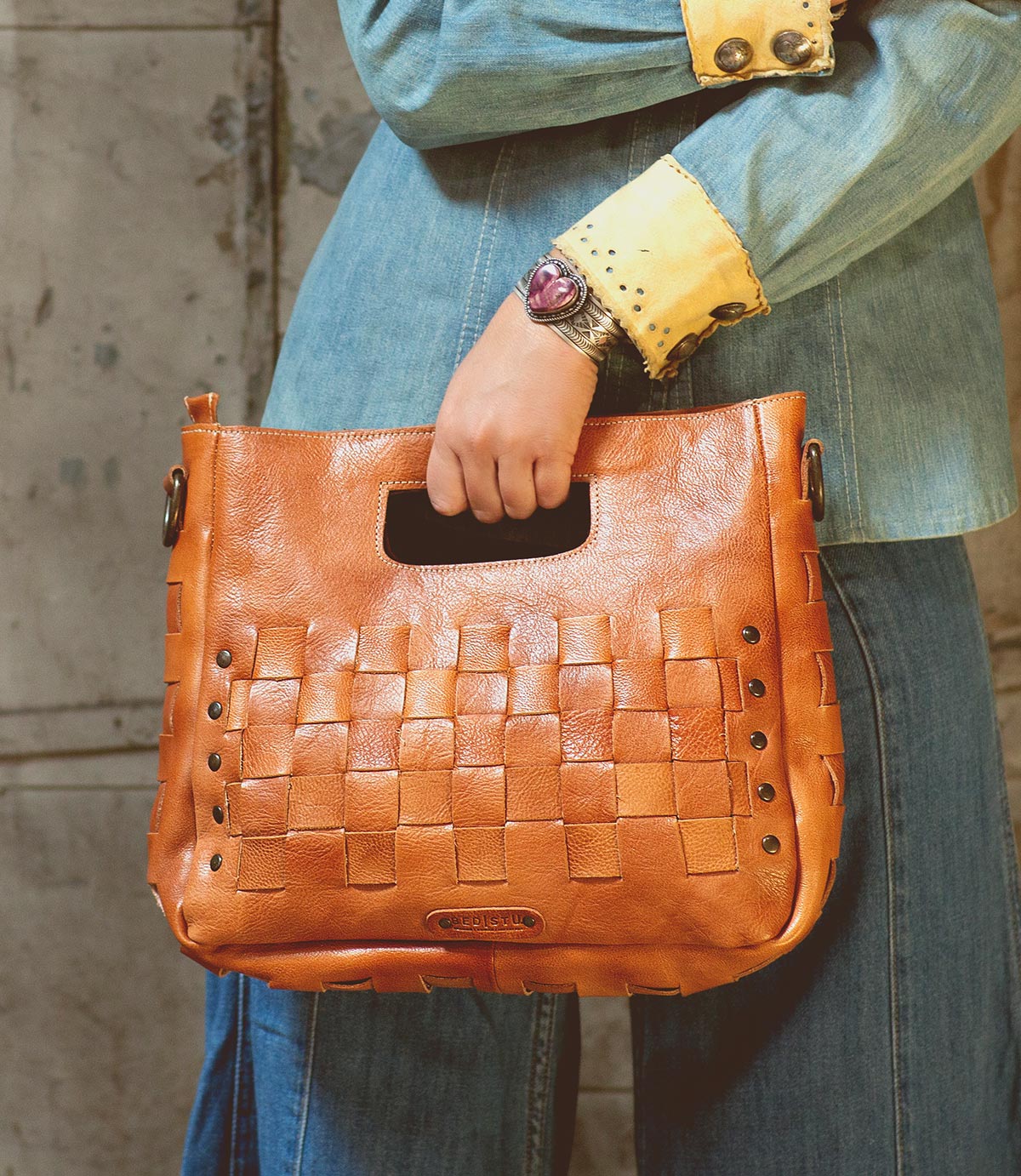 A woman is holding an adjustable handwoven Orchid handbag by Bed Stu.