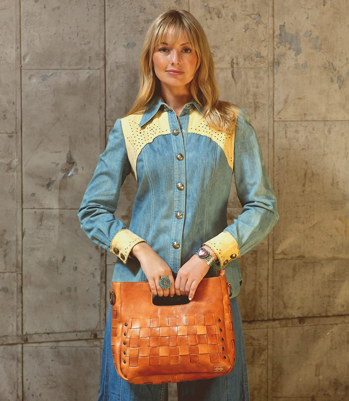 A woman in a denim shirt holding a tan Orchid purse, featuring an adjustable handwoven Bed Stu handbag.