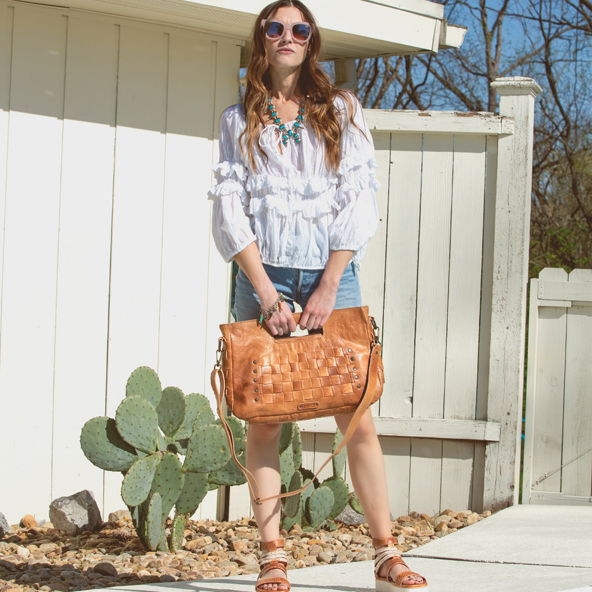 A woman in a white top and shorts holding a Bed Stu Orchid L tan purse.
