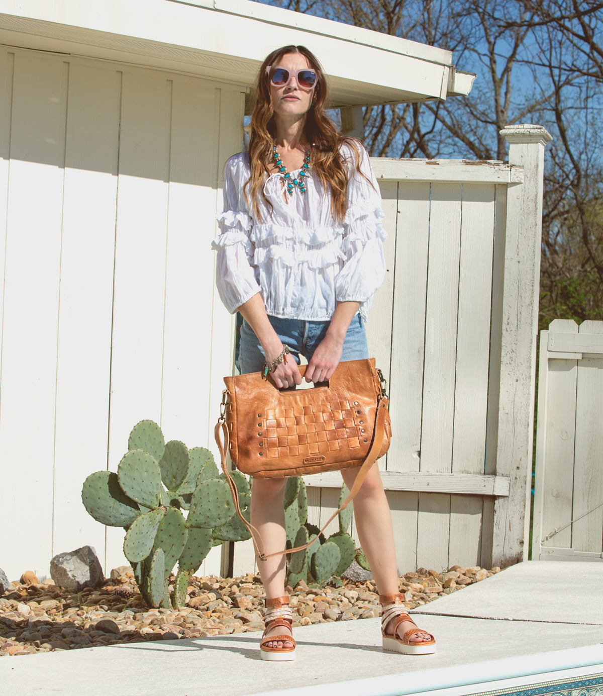 A woman in a white top and shorts holding a Bed Stu Orchid L tan purse.