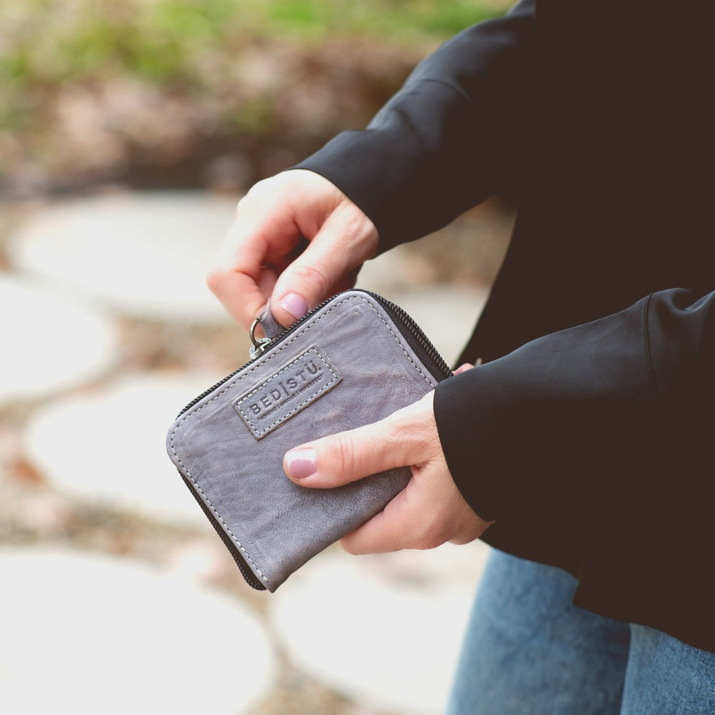 A woman holding a grey Bed Stu Ozzie wallet on a sidewalk.