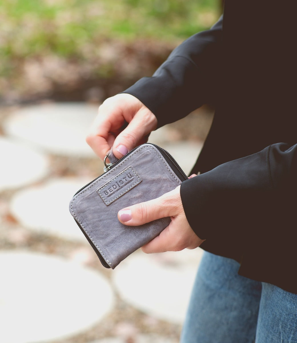 A woman holding a grey Bed Stu Ozzie wallet on a sidewalk.