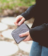 A woman holding a grey Bed Stu Ozzie wallet on a sidewalk.
