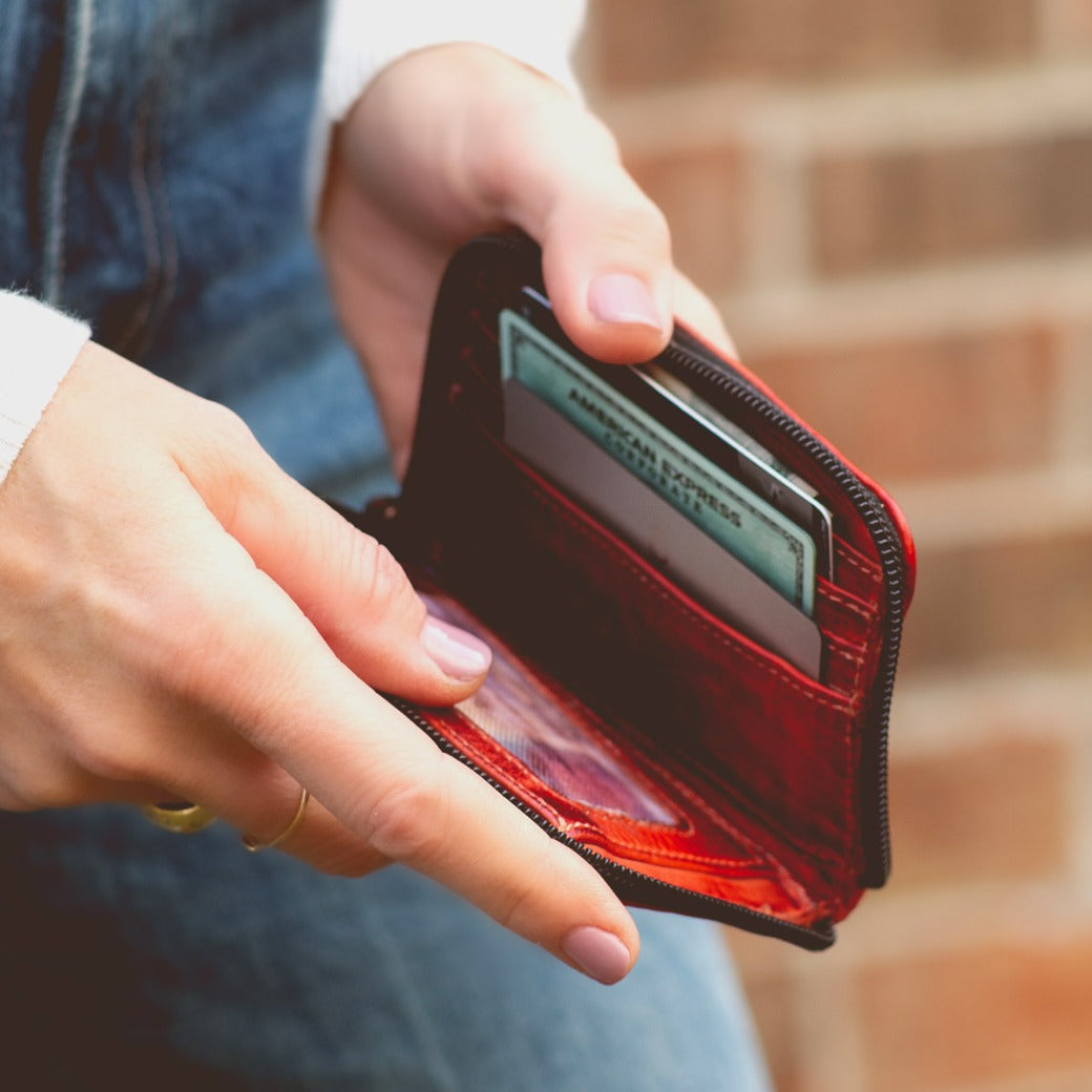 A woman holding a red Ozzie wallet by Bed Stu with a credit card in it.