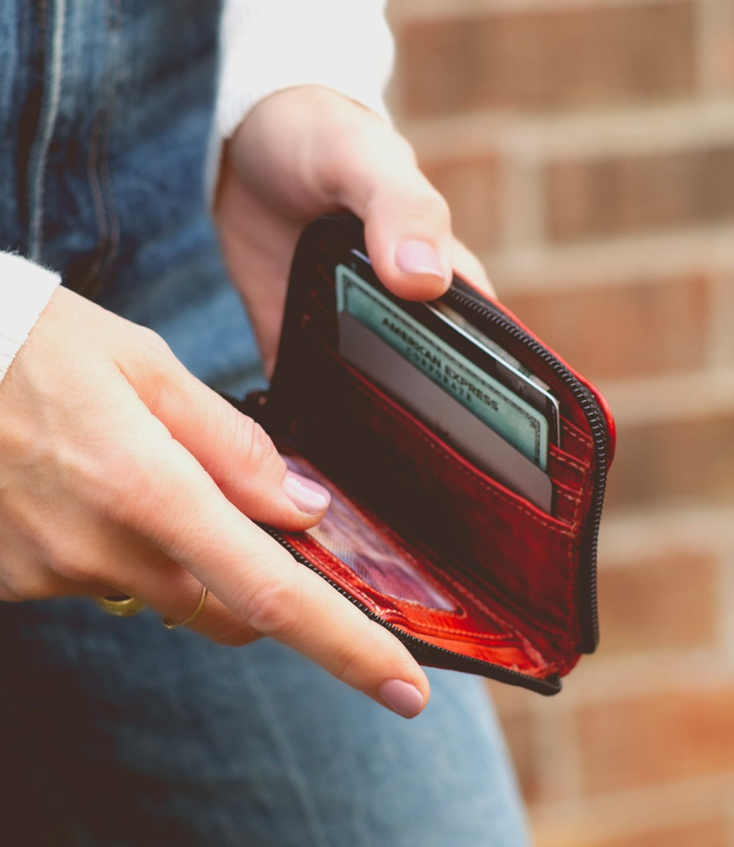 A woman holding a red Ozzie wallet by Bed Stu with a credit card in it.