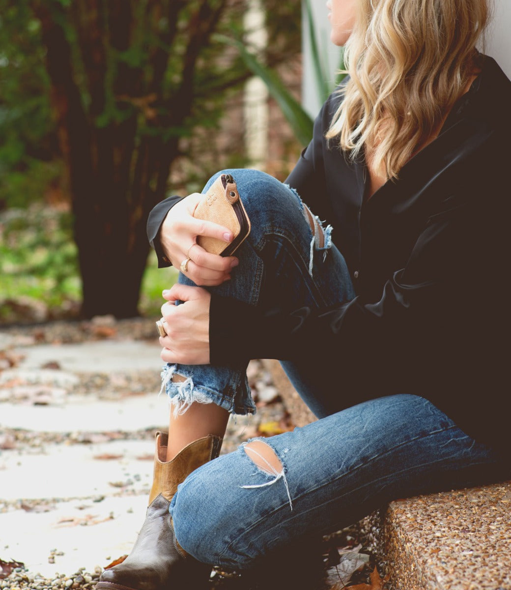 A woman wearing Ozzie jeans and Bed Stu boots sitting on a step.