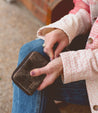 A woman holding an Ozzie wallet by Bed Stu while sitting on a bench.