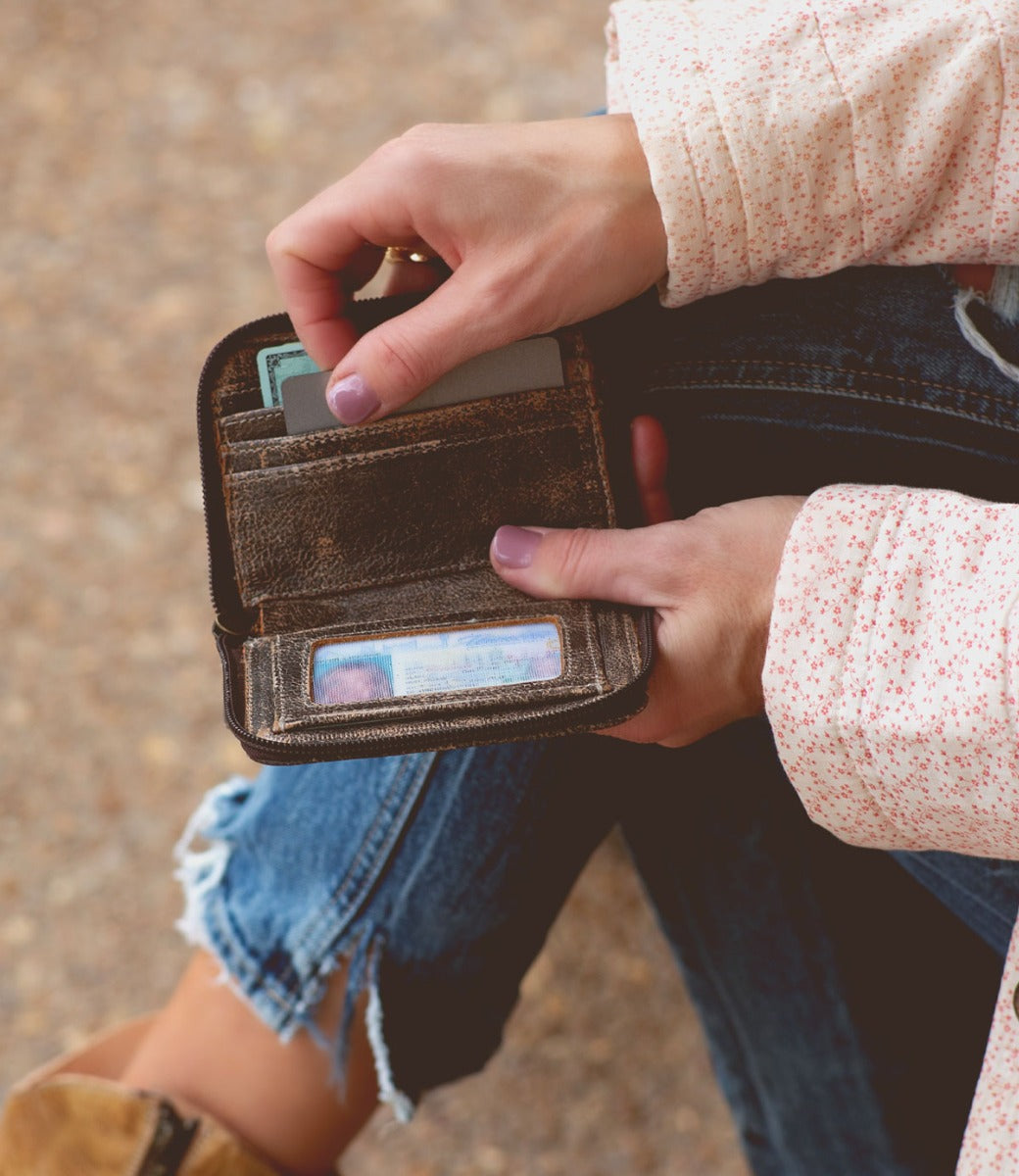 A woman is holding an Ozzie wallet while sitting on the ground.