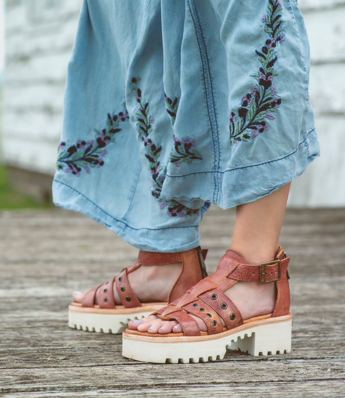 A woman wearing the Pacifica sandals from Bed Stu on a wooden deck.