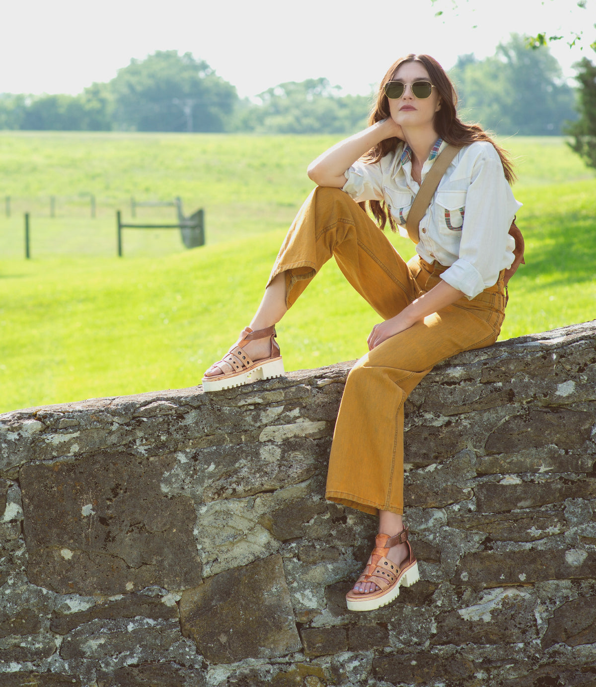 A woman is sitting on a stone wall wearing the Pacifica sandals by Bed Stu.