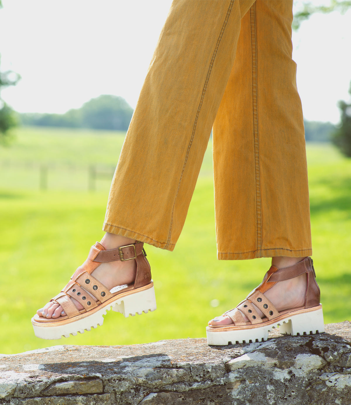 A woman wearing Bed Stu Pacifica sandals standing on a stone wall.