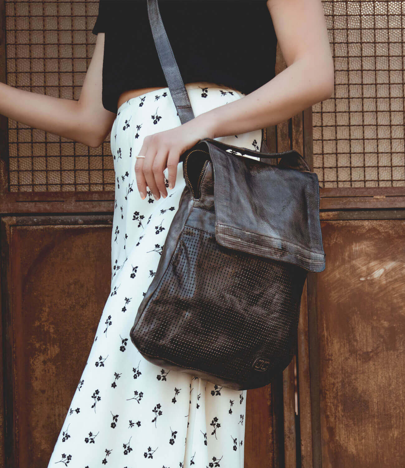 A woman holding a Bed Stu Patsy black leather bag in front of a wooden door.