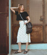 A woman leaning against a wall wearing a black crop top and Bed Stu's Patsy floral midi skirt.