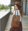 A woman wearing a hat and skirt is holding a Bed Stu Patsy brown leather bag.