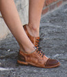 A woman's legs in a pair of Bed Stu Plio brown oxford shoes.