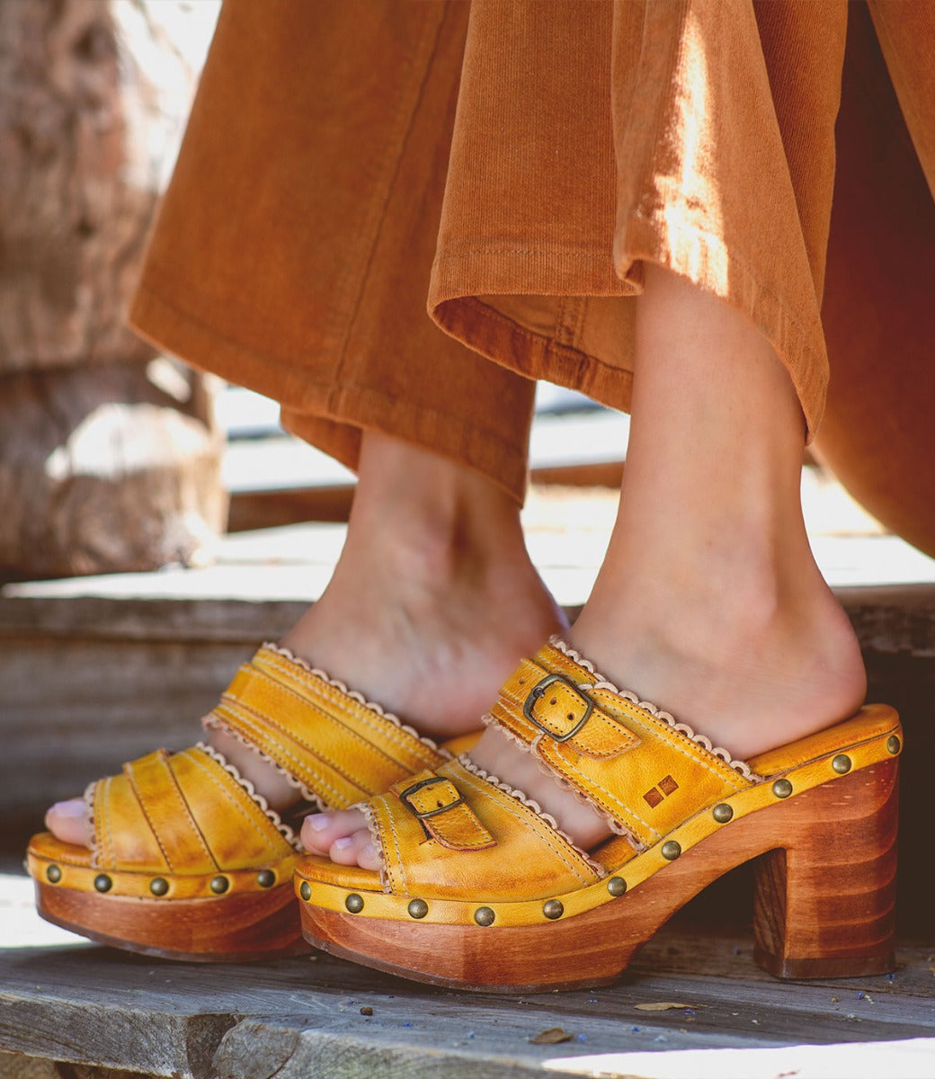 A woman wearing yellow Bed Stu sandals on a wooden deck.