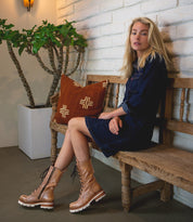 A woman sitting on a wooden bench wearing Bed Stu Posh boots.