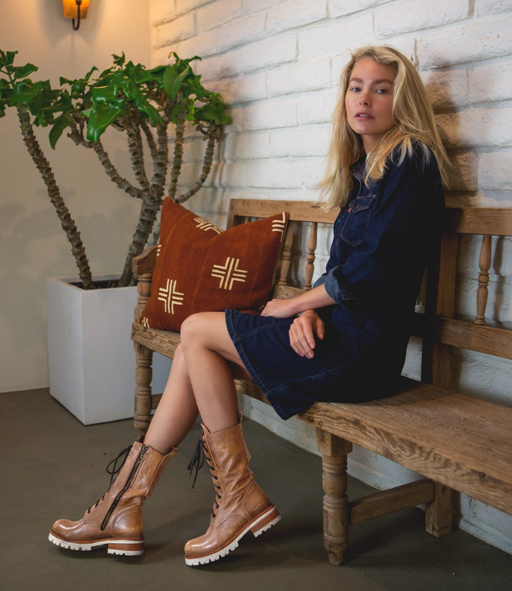 A woman sitting on a wooden bench wearing Bed Stu Posh boots.