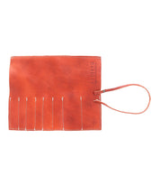 A flat, orange Bed Stu Prepped Leather Wrap with a strap and slots for storing artist tools.