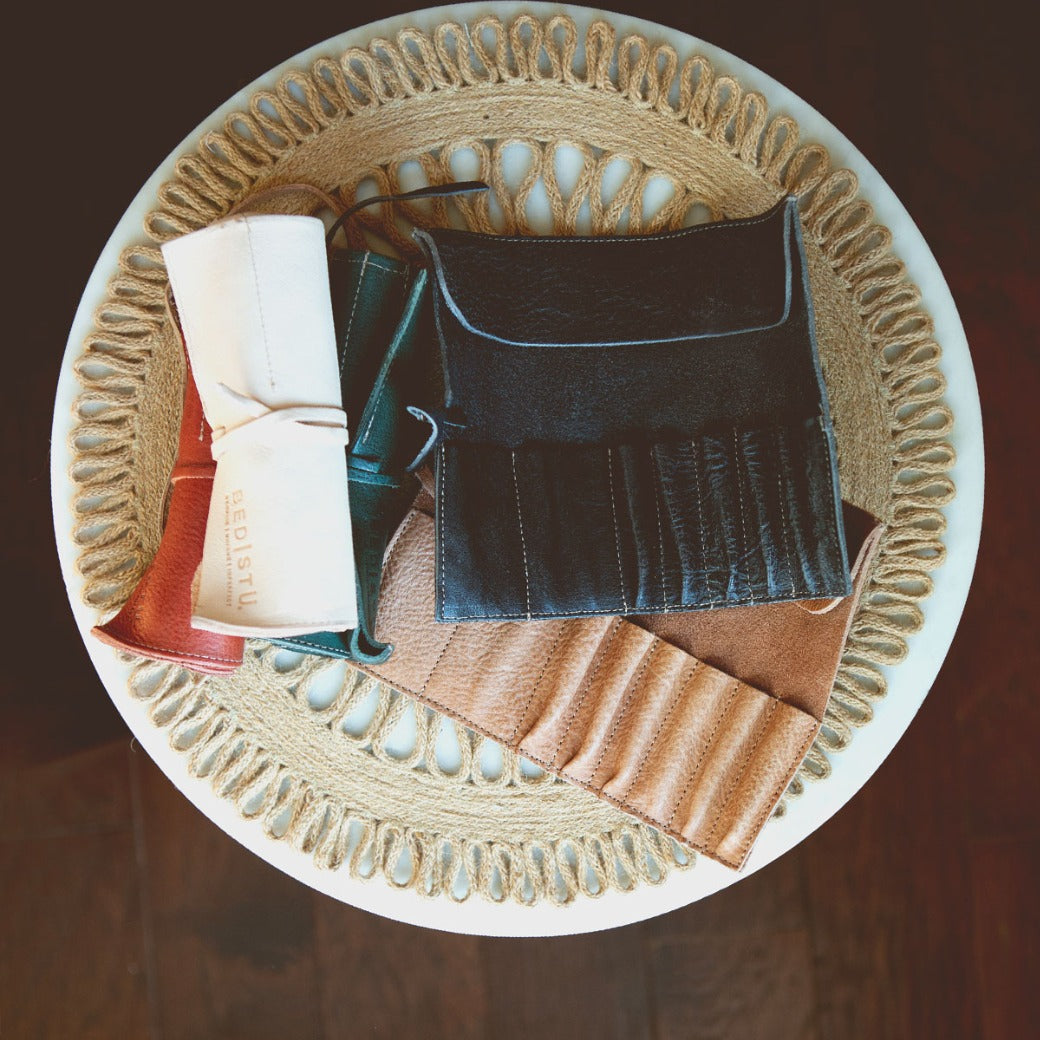 A circular woven mat on a round table in the Leather Shoppe holds neatly arranged Prepped Leather Wraps by Bed Stu in various colors.