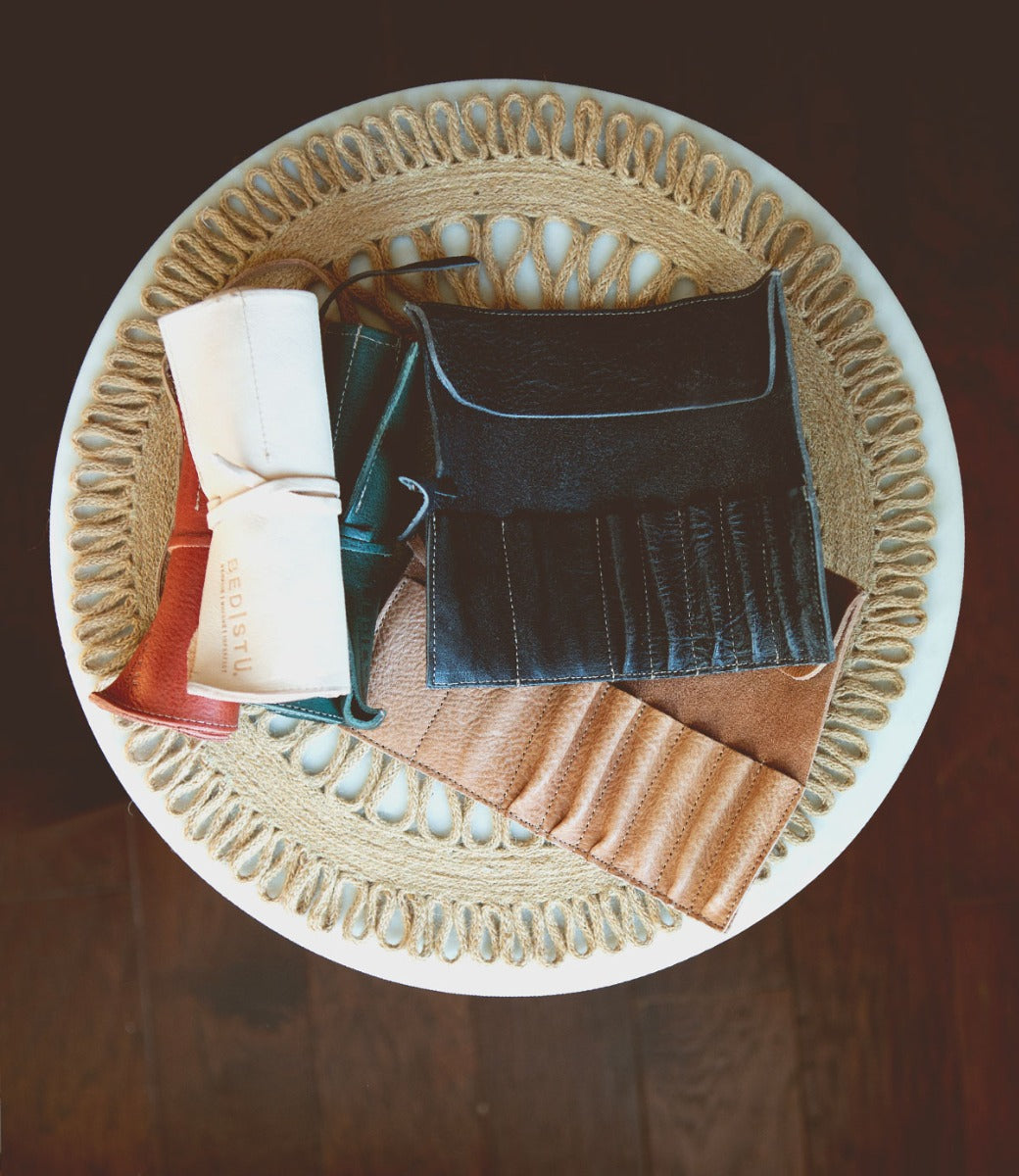 A circular woven mat on a round table in the Leather Shoppe holds neatly arranged Prepped Leather Wraps by Bed Stu in various colors.