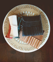 A circular woven mat on a round table in the Leather Shoppe holds neatly arranged Prepped Leather Wraps by Bed Stu in various colors.