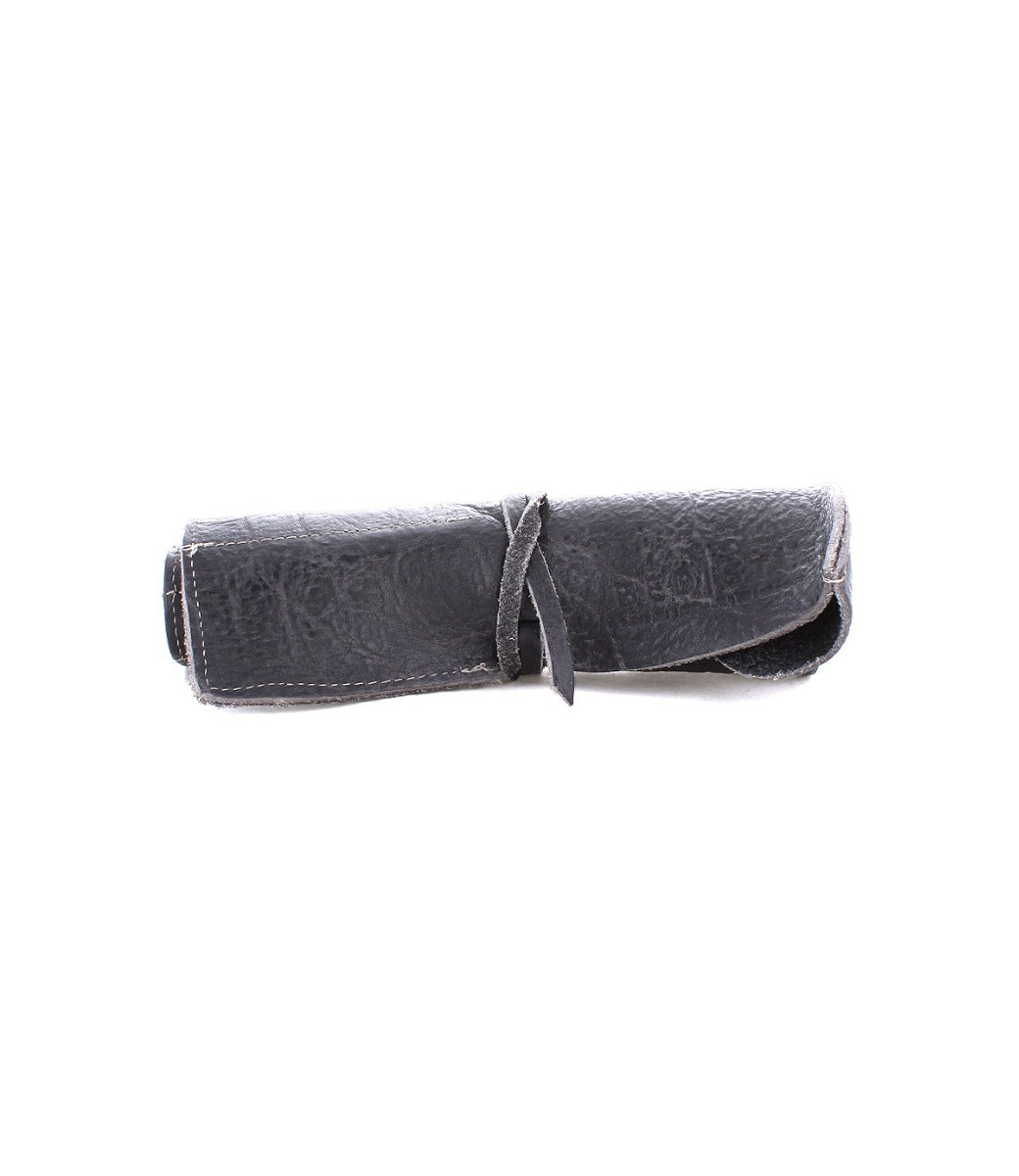 A rolled-up black leather pouch, perfect for artist tools, is secured with a matching leather strap from the renowned Bed Stu Prepped Leather Wrap.