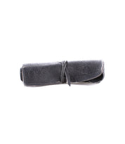 A rolled-up black leather pouch, perfect for artist tools, is secured with a matching leather strap from the renowned Bed Stu Prepped Leather Wrap.