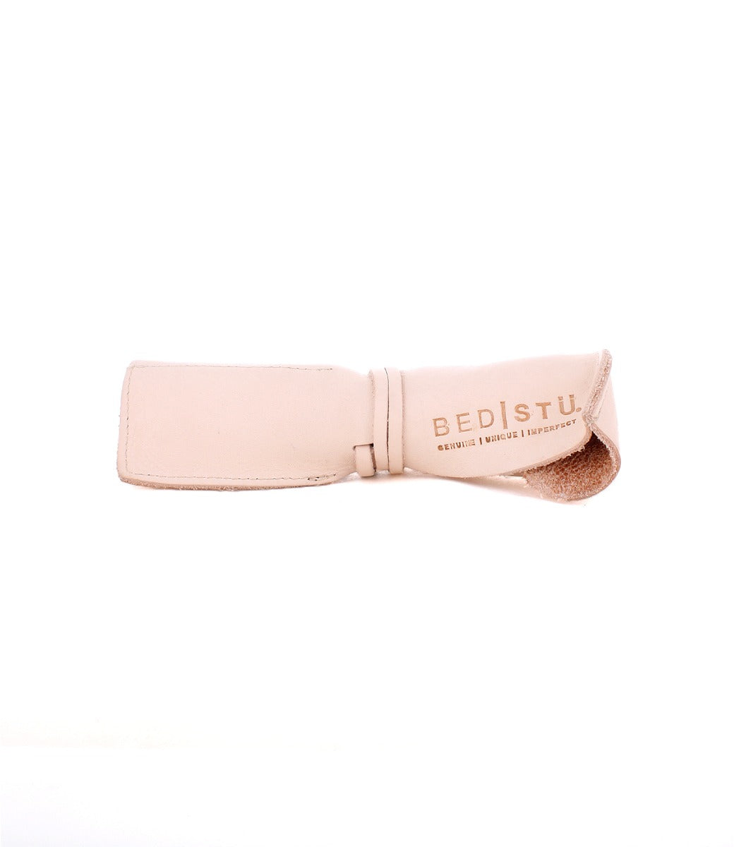 A beige leather wrap with the text "Bed Stu" followed by "Genuine. Unique. Imperfect." printed on it, crafted from the finest materials at our Leather Shoppe.