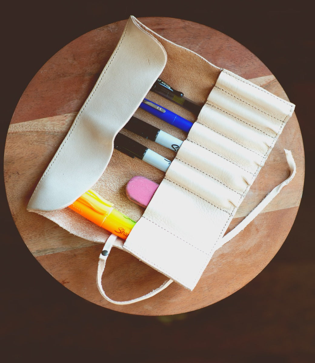 A Prepped Leather Wrap from Bed Stu, containing a highlighter, markers, pens, and an eraser, rests gracefully on a wooden surface.