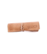 A rolled-up beige leather wrap with a strap, featuring the Bed Stu brand name and text, perfect for organizing artist tools.
