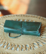 A green Bed Stu Prepped Leather Wrap sits on a woven circular table mat, resembling a piece straight from an artisanal Leather Shoppe.